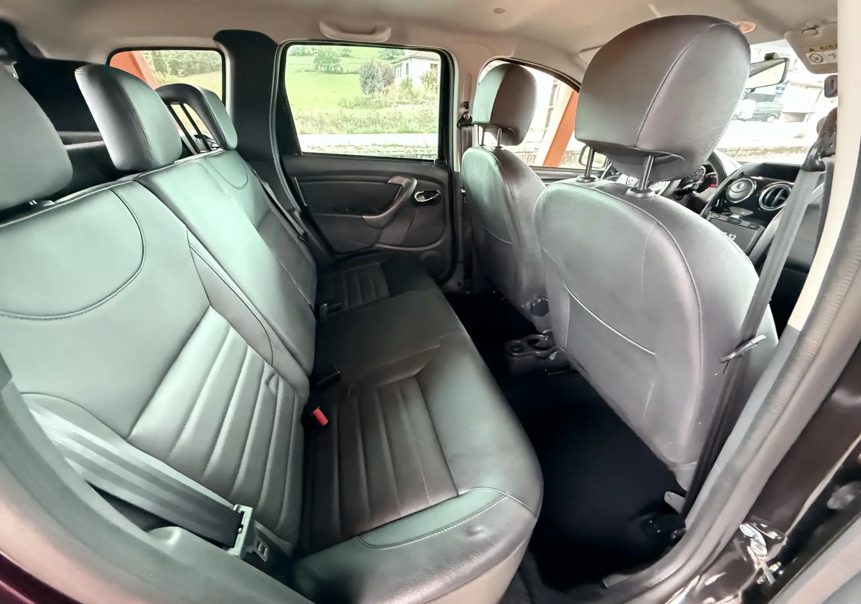 Vue intérieure arrière côté droit du Dacia Duster 2017 noir métal, montrant les sièges en cuir noir et les portières ouvertes.