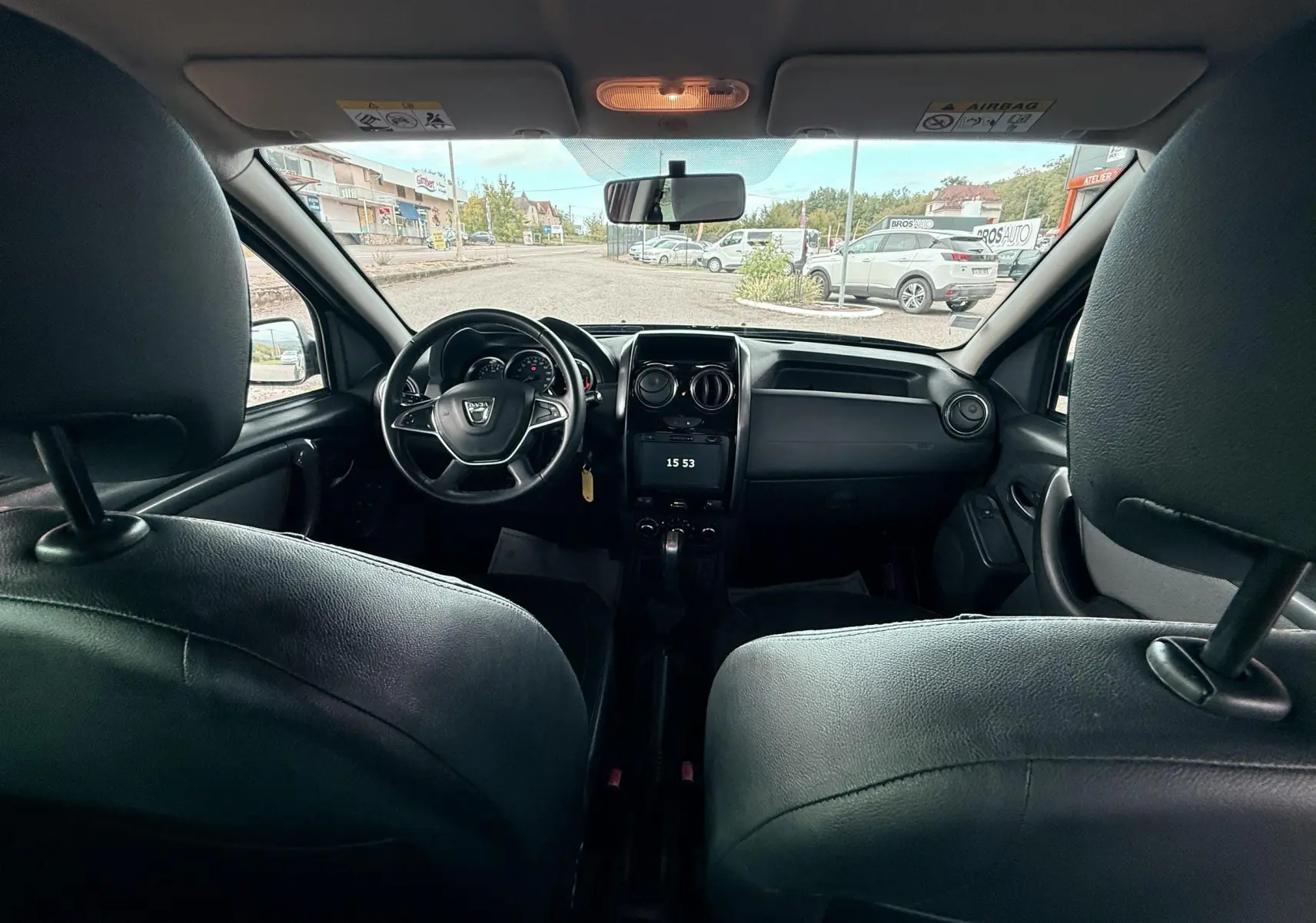 Intérieur noir cuir du Dacia Duster 2017 vu de l'arrière, tableau de bord et volant au centre, écran tactile allumé.