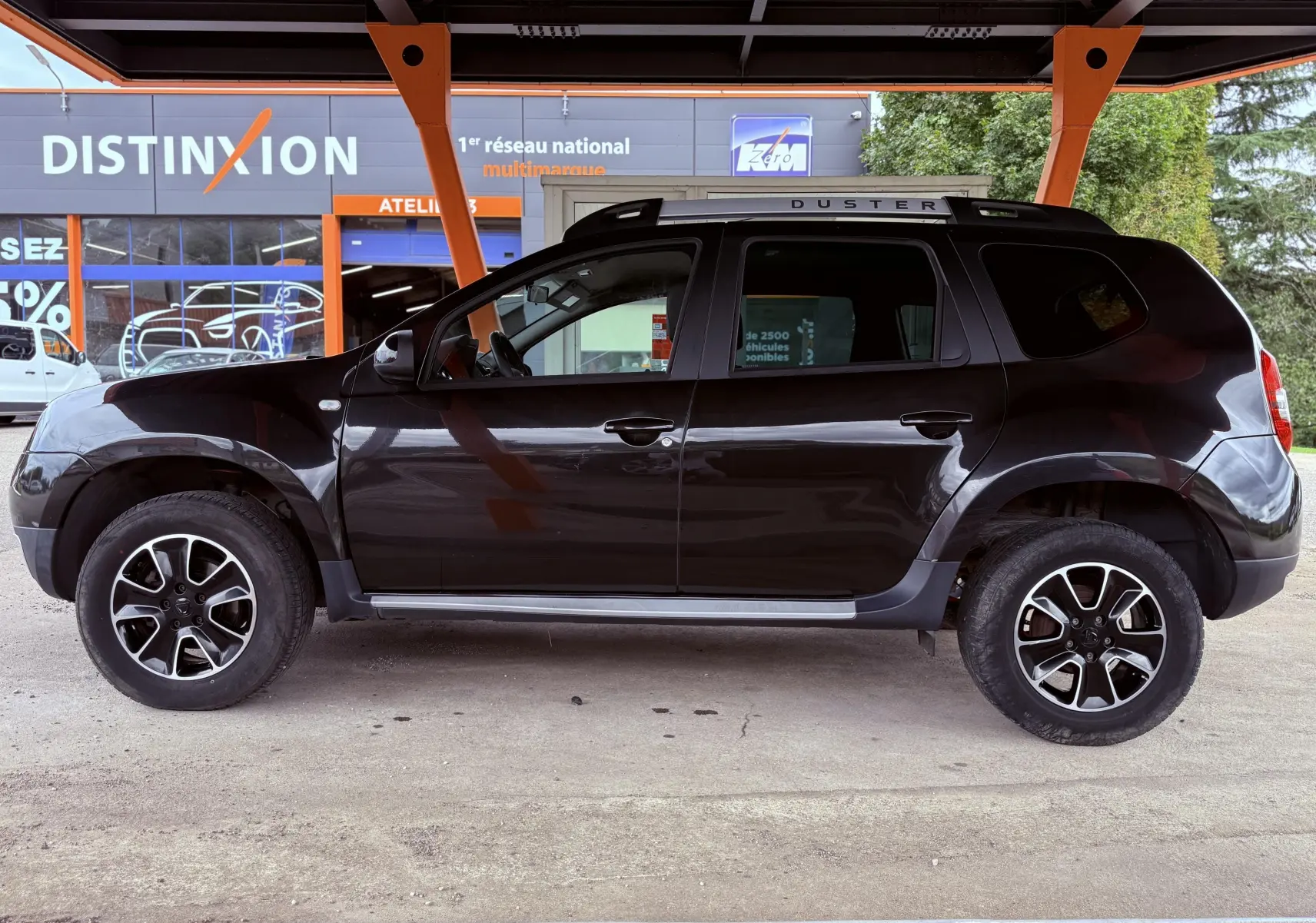 Profil côté gauche d'un Dacia Duster noir métal 2017 avec jantes biton et barres de toit marquées DUSTER.