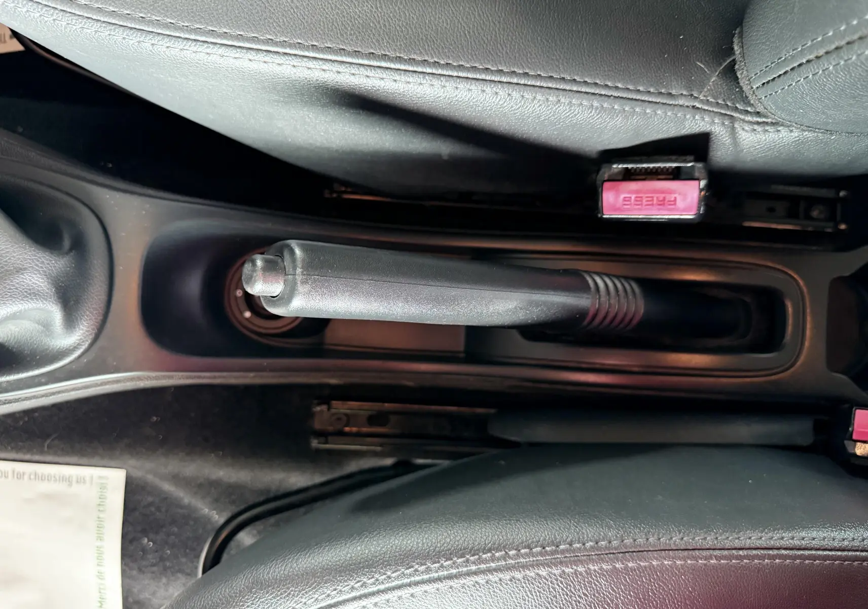 Le levier de frein à main noir et les ceintures de sécurité rouges entre les sièges en cuir noir du Dacia Duster.