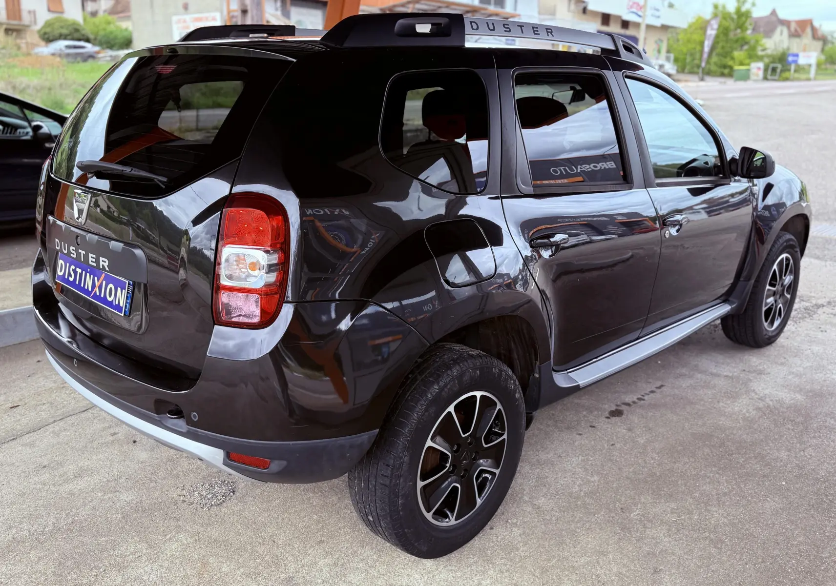 Vue 3/4 arrière droite du Dacia Duster noir métal, avec jantes bi-ton et barres de toit marquées DUSTER.