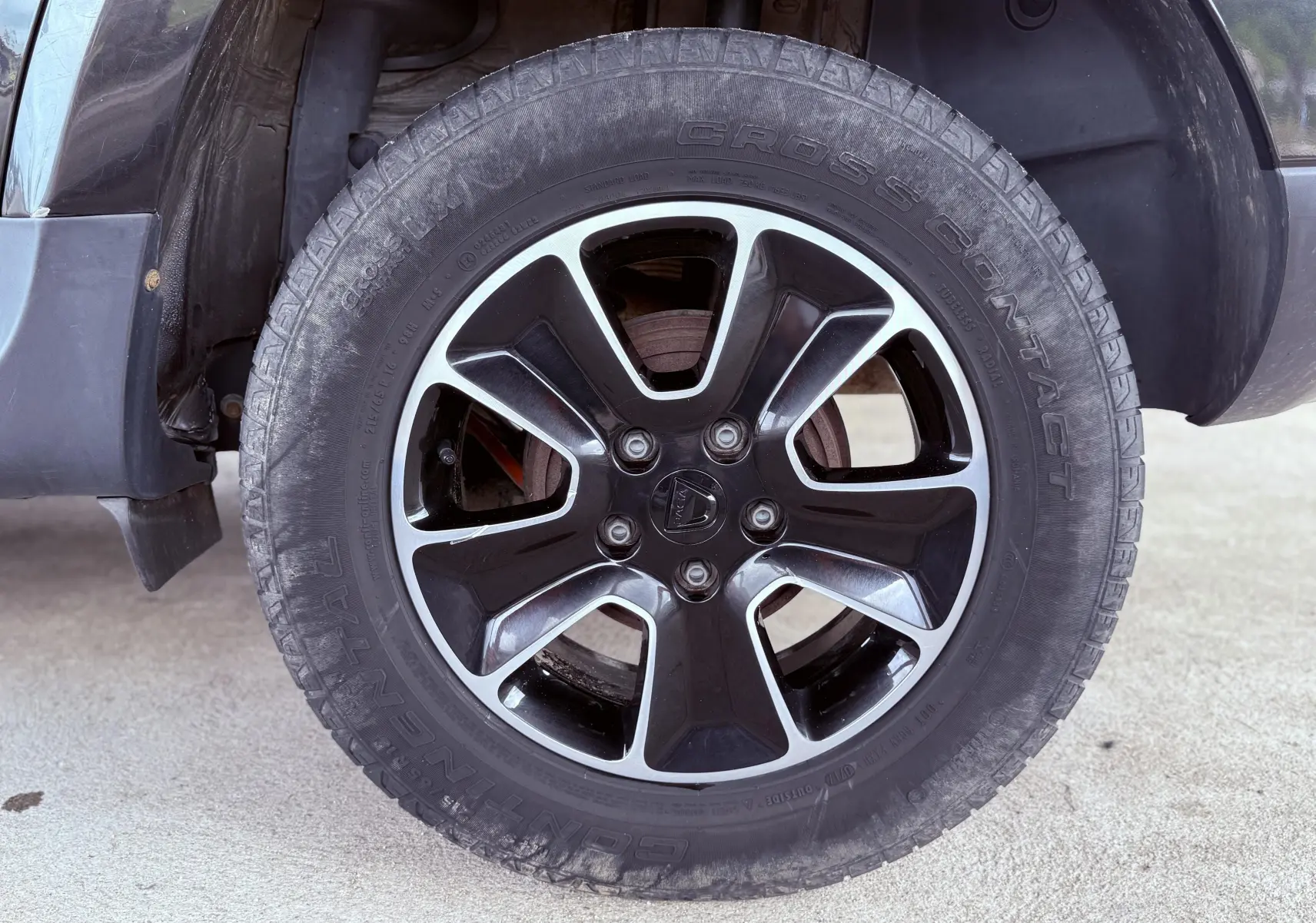 Gros plan sur la roue avant gauche du Dacia Duster noir métal, mettant en valeur la jante alliage bicolore et le pneu Continental.