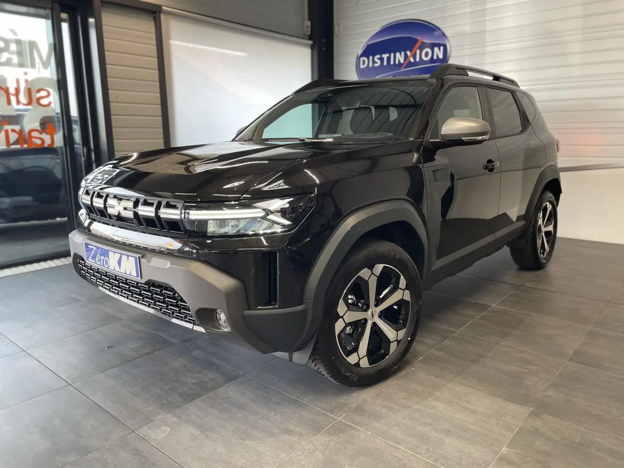 SUV Dacia Duster 2025 noir métallisé vu en 3/4 avant droit avec jantes alliage et barres de toit noires