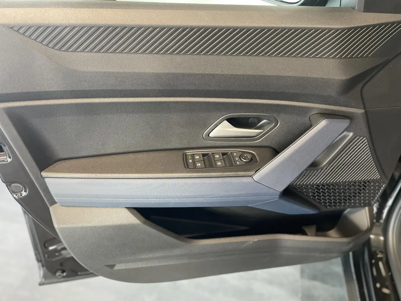 Intérieur côté gauche de la porte avant d'un Dacia Duster 2025 noir métallisé avec commandes de vitres et accoudoir Denim bleu.