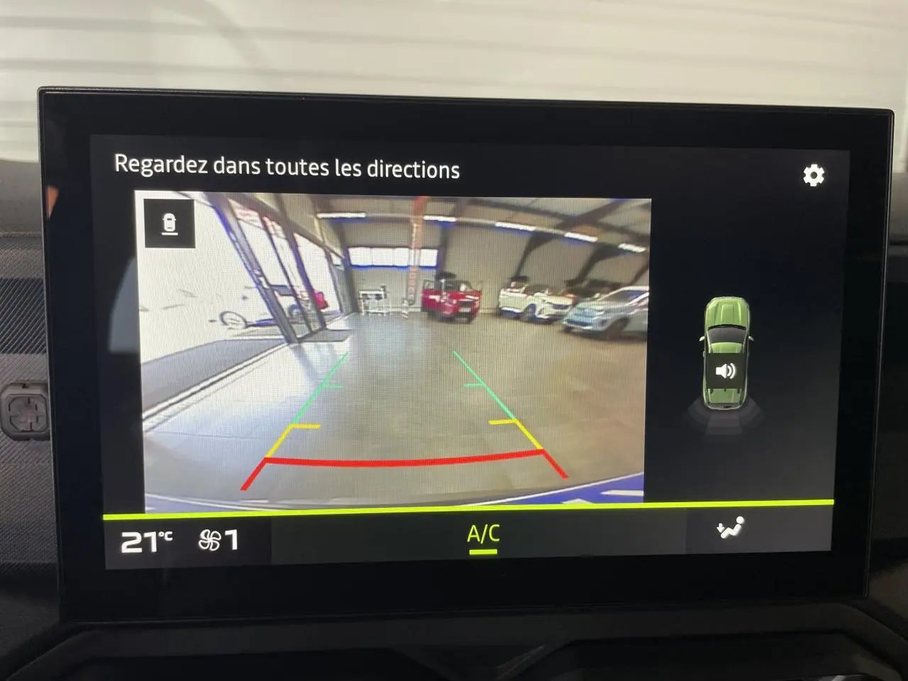 Écran de caméra de recul du Dacia Duster 2025 montrant l'arrière dans un garage avec plusieurs véhicules stationnés.