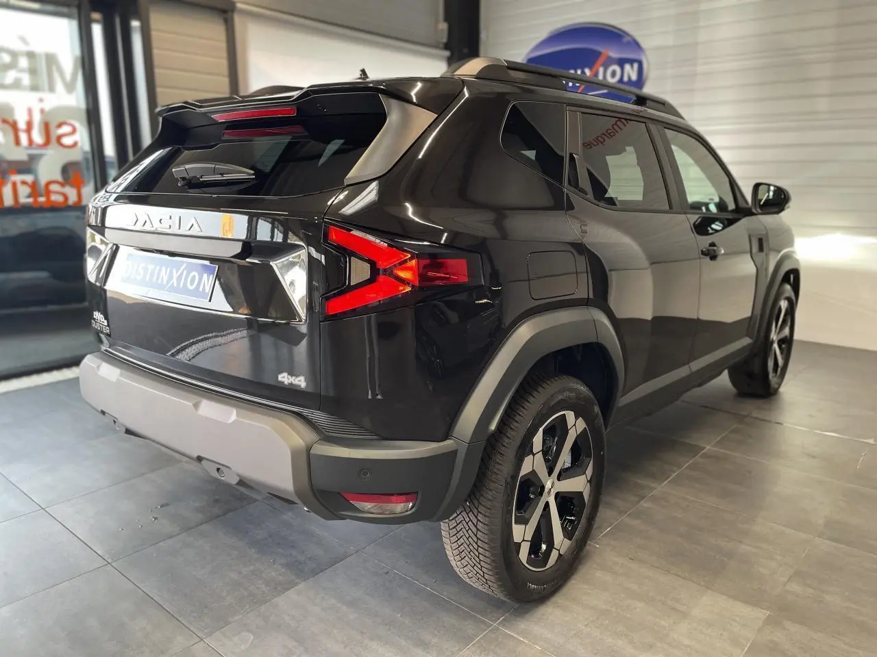 Vue 3/4 arrière droite du SUV Dacia Duster 2025 noir métallisé avec jantes alliage et barres de toit noires.