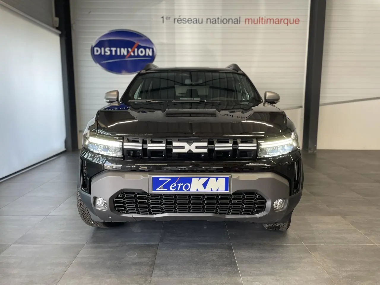 Vue frontale d'un Dacia Duster 2025 noir métallisé avec calandre marquée et plaque Zero KM visible.