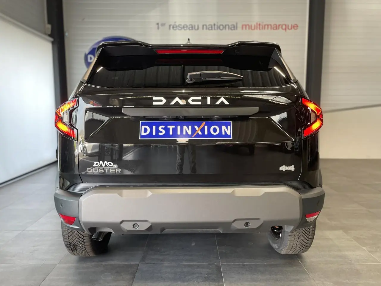 Vue arrière d'un Dacia Duster 2025 noir métallisé avec logo DACIA lumineux et badge 4x4 visible.