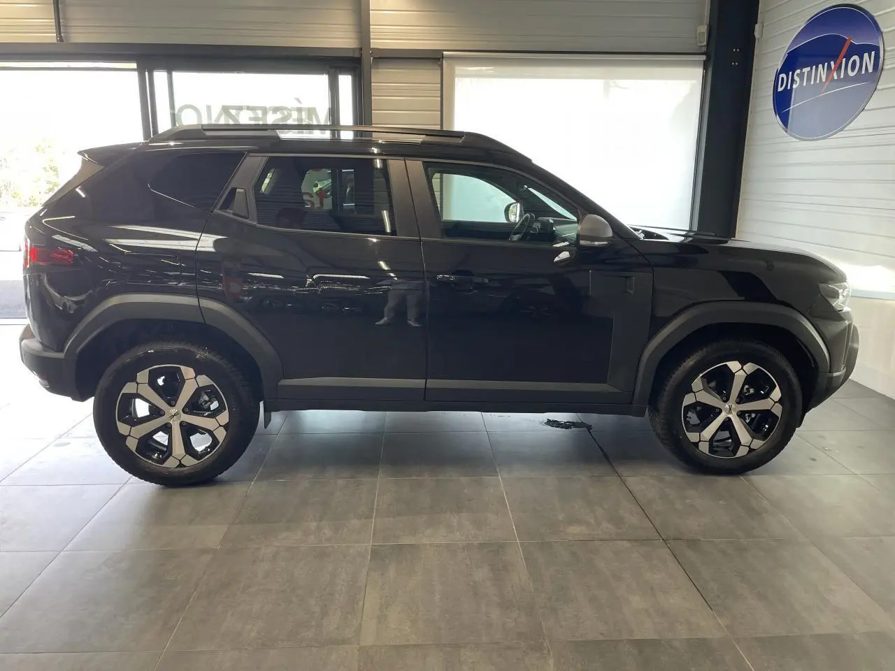 Profil côté gauche du SUV Dacia Duster 2025 noir métallisé avec jantes alliage 18 pouces et barres de toit noires.