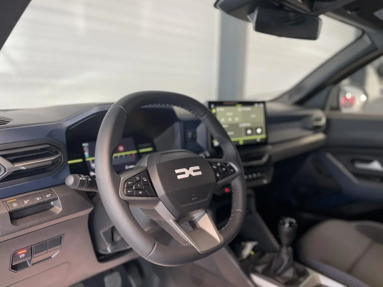 Intérieur du Dacia Duster 2025 vu côté conducteur, volant noir avec logo DC et écran tactile central visible.