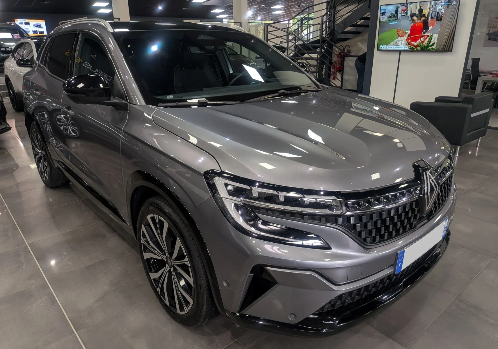 Renault Austral E-Tech gris schiste en 3/4 avant droit, avec calandre noire à damier et jantes bicolores.
