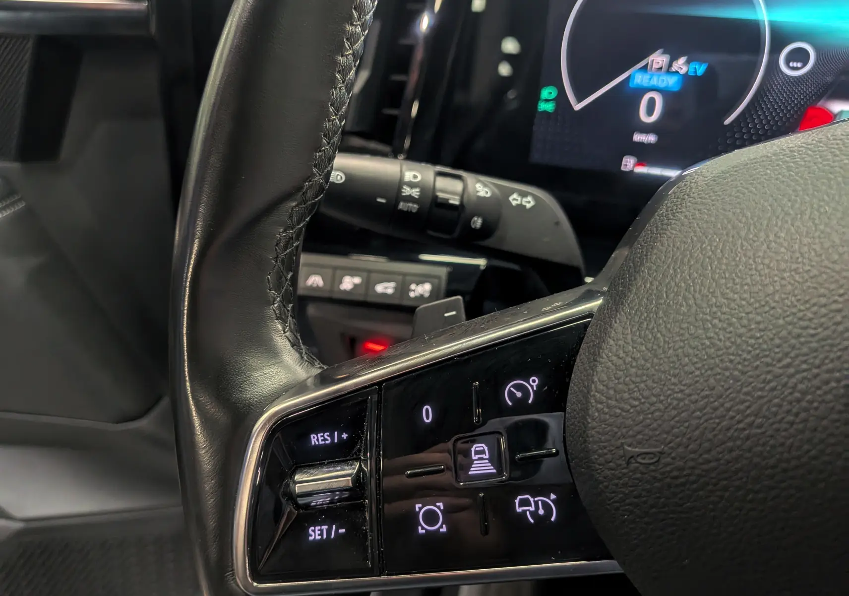 Gros plan sur les commandes au volant en cuir noir du Renault Austral E-TECH 2024, affichage digital en arrière-plan.
