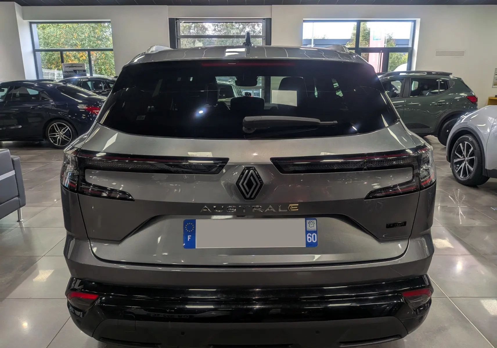 Vue arrière d'un Renault Austral gris schiste en showroom, avec feux arrière fins et logo central lumineux.