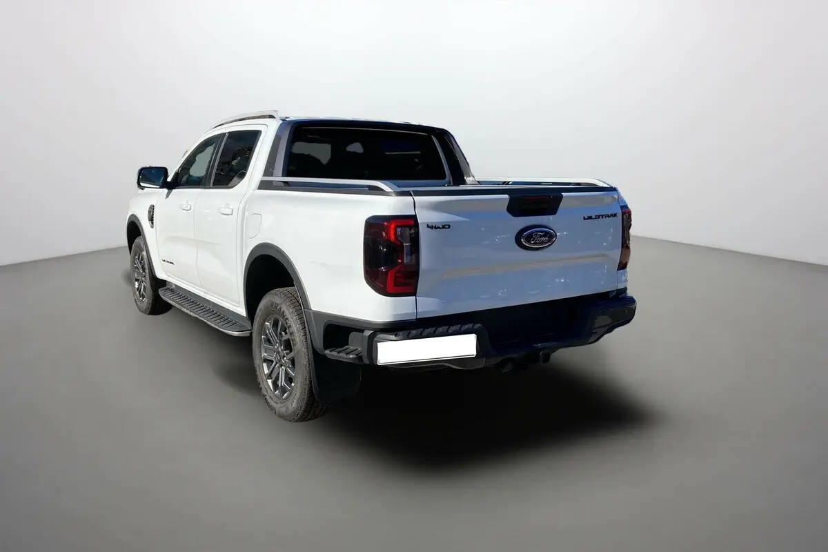 Ford Ranger 2.0 205 Wildtrak Plus blanc glacier vu en 3/4 arrière droit avec logo et feux arrière distinctifs.
