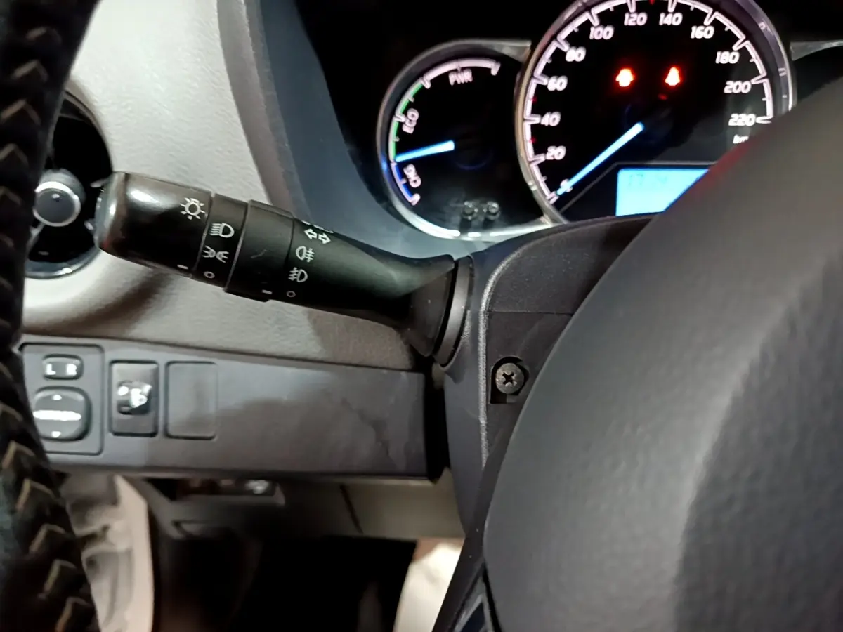 Vue rapprochée du commodo d’éclairage à gauche du volant noir dans l’habitacle d’une Toyota Yaris hybride.