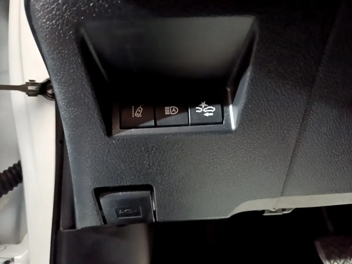 Gros plan sur les commandes de sécurité sous le tableau de bord d'une Toyota Yaris blanche, version hybride.