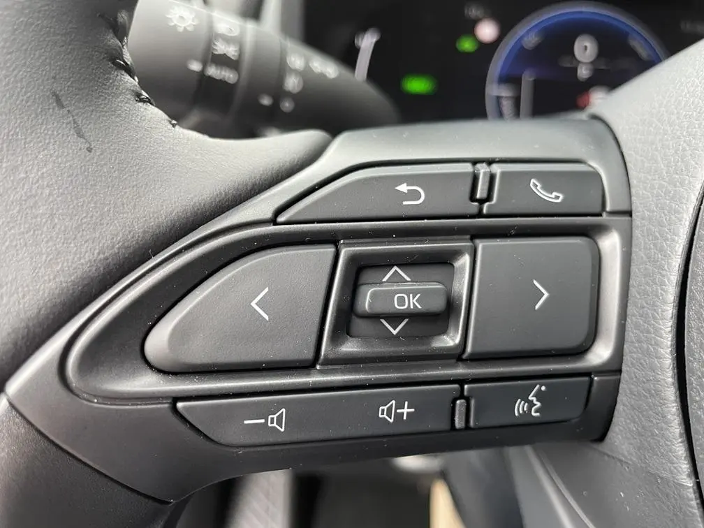 Gros plan sur les commandes multifonctions noires du volant cuir d'une Toyota Yaris Cross 1.5 Hybrid 130H Design.