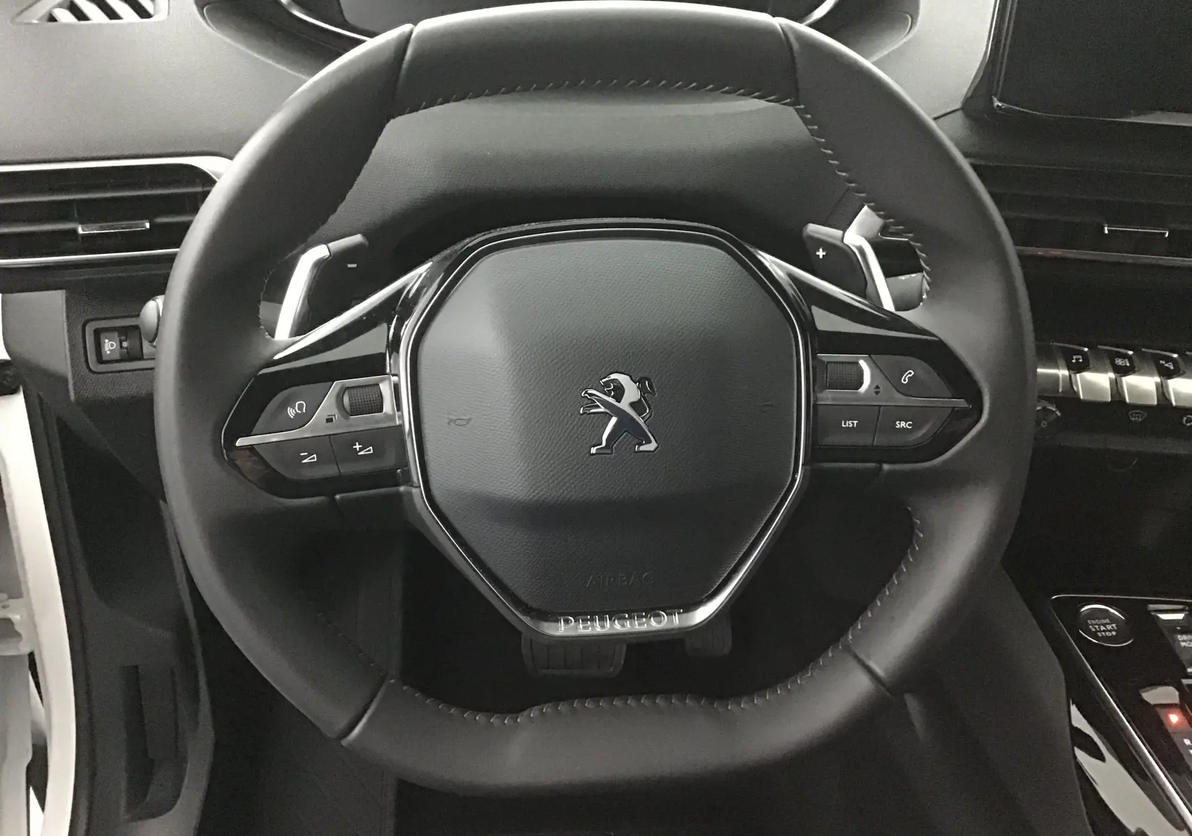 Vue rapprochée du volant cuir noir du Peugeot 5008 2024 avec commandes intégrées et logo central chromé.