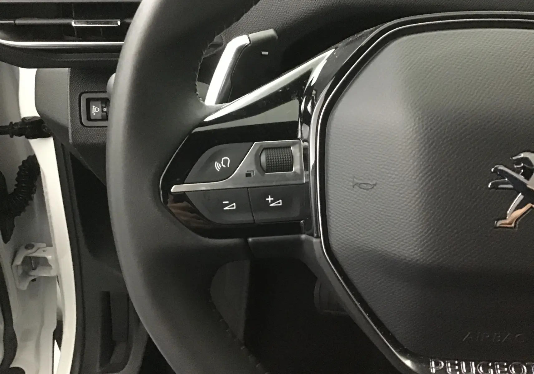 Gros plan sur le volant cuir noir du Peugeot 5008 blanc nacré, montrant les commandes audio et le logo lion central.
