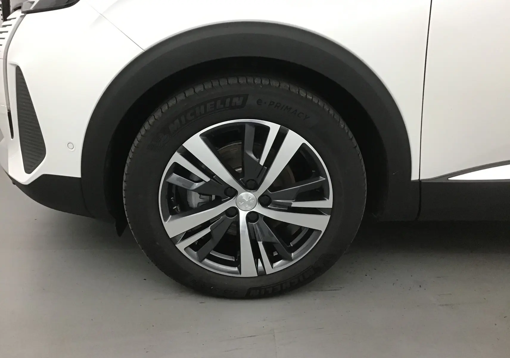 Gros plan sur la roue avant gauche d’un Peugeot 5008 blanc nacré avec jante alliage bicolore et pneu Michelin.