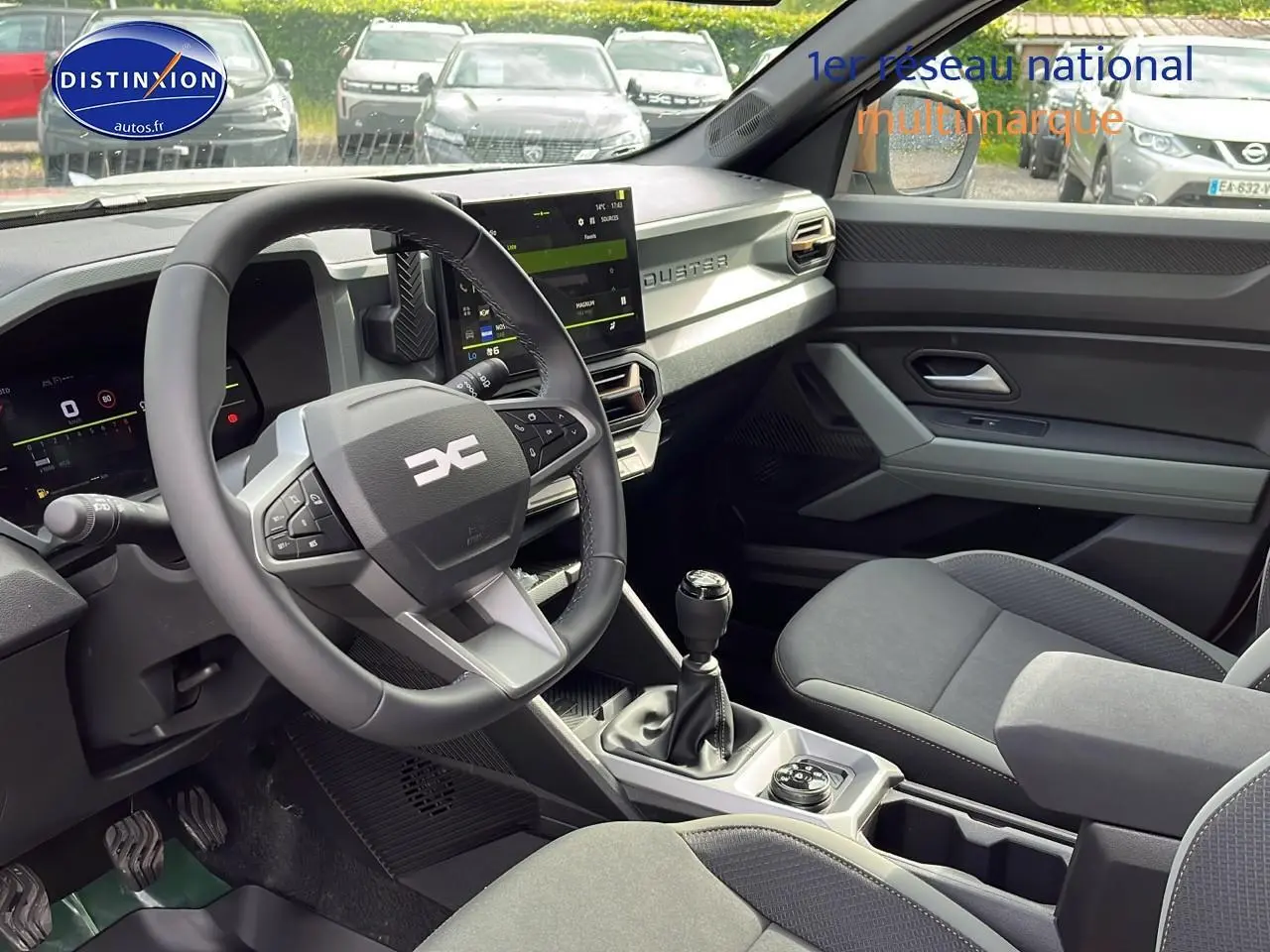 Intérieur du Dacia Duster 2025 avec volant multifonction, écran tactile et sièges gris, vu côté conducteur.