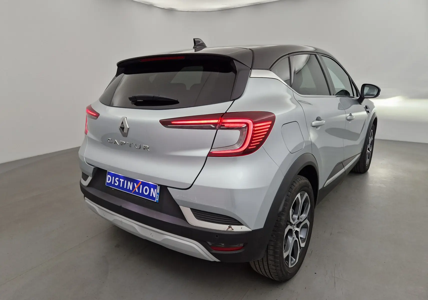 Vue 3/4 arrière droite du Renault Captur 2024 gris Highland avec toit noir et feux arrière LED allumés.