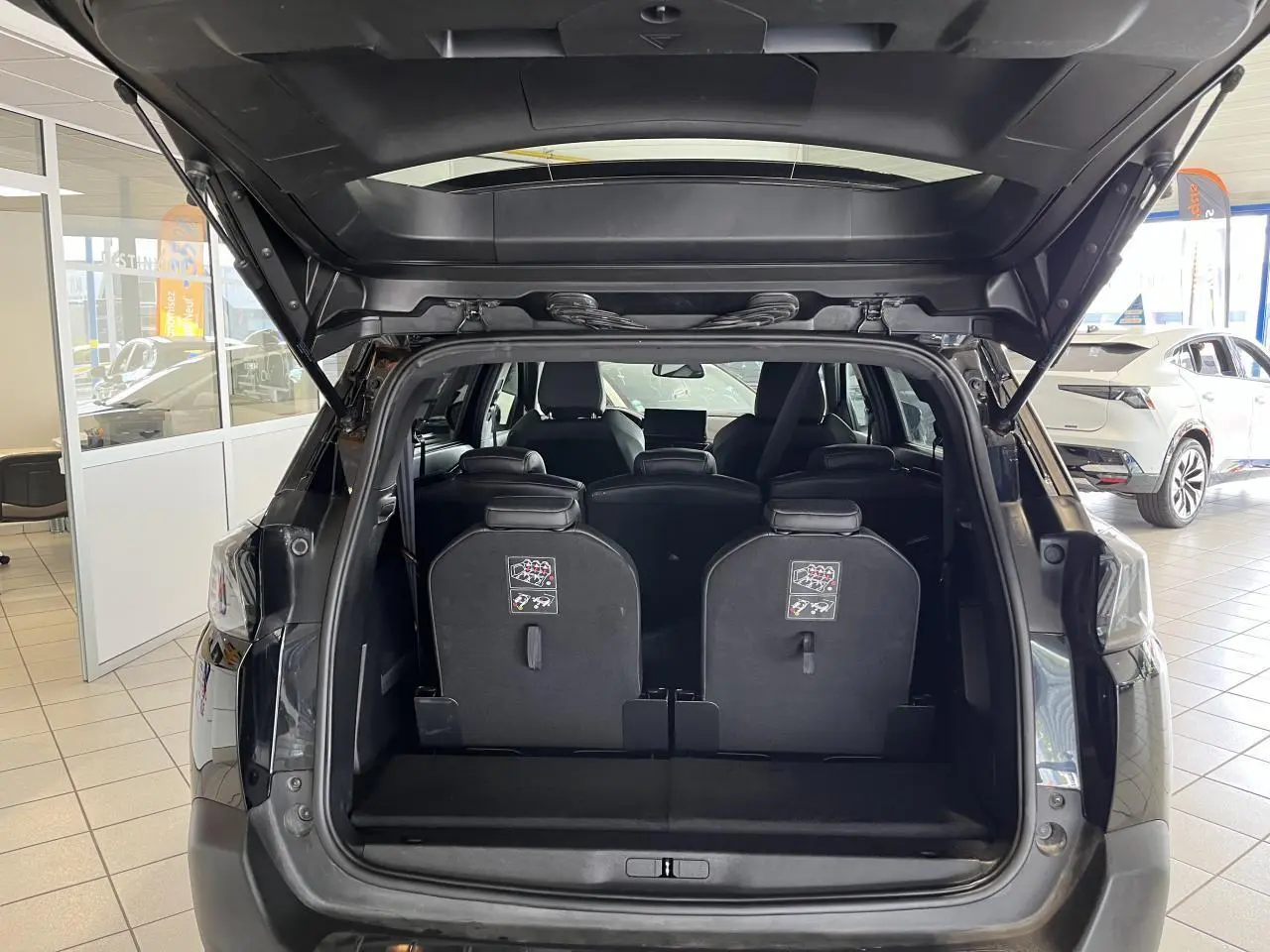 Coffre ouvert d'un Peugeot 5008 noir métallisé 2024, montrant les sièges arrière escamotables et l'habitacle intérieur.