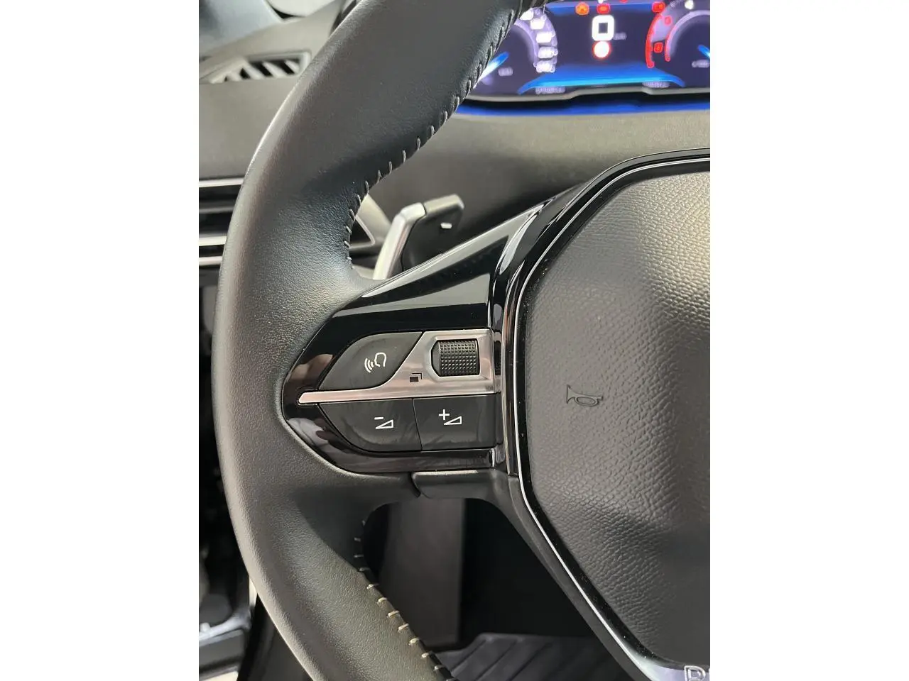 Gros plan sur le volant noir cuir du Peugeot 5008 2024 avec commandes intégrées et tableau de bord numérique lumineux.