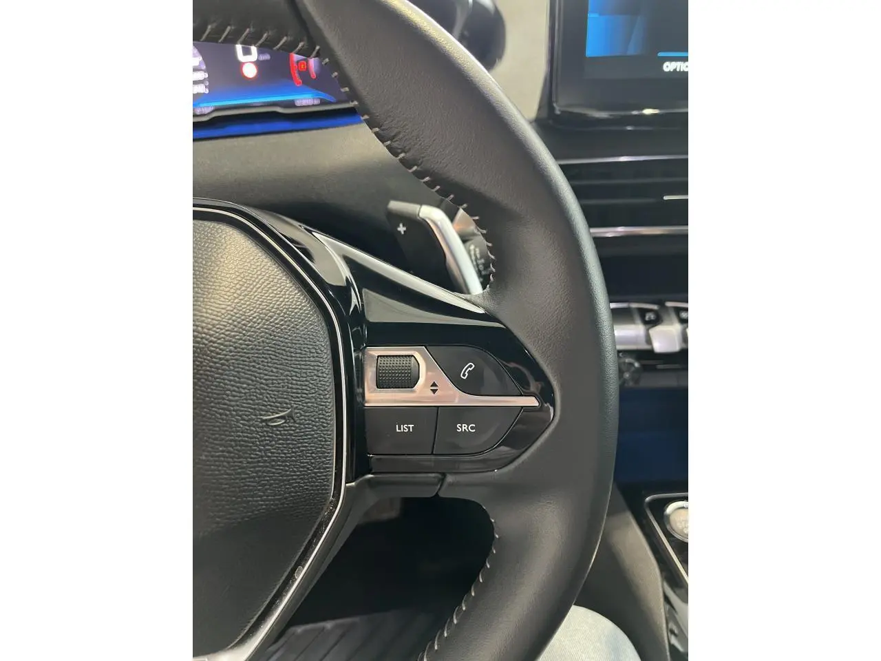 Gros plan sur le volant noir du Peugeot 5008 2024 avec commandes intégrées et tableau de bord numérique partiel visible.