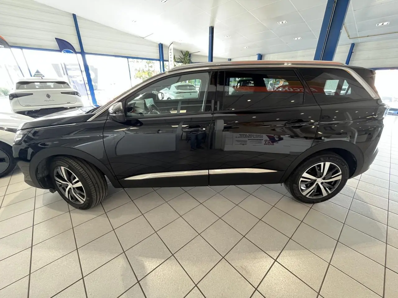 Profil côté gauche du Peugeot 5008 noir métallisé avec jantes alliage bicolores dans un showroom lumineux