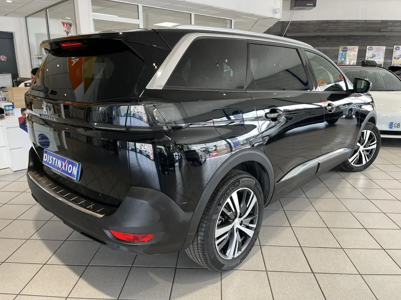 Peugeot 5008 noir métallisé vue 3/4 arrière droit en showroom avec vitres surteintées et jantes alliage bi-ton.