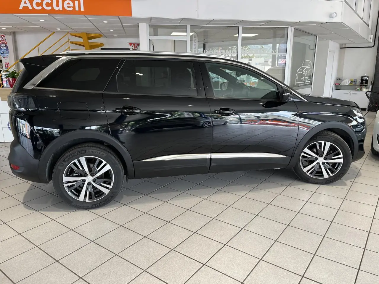 Profil côté gauche d'un Peugeot 5008 noir métallisé 2024 avec jantes alliage bi-ton dans un showroom.