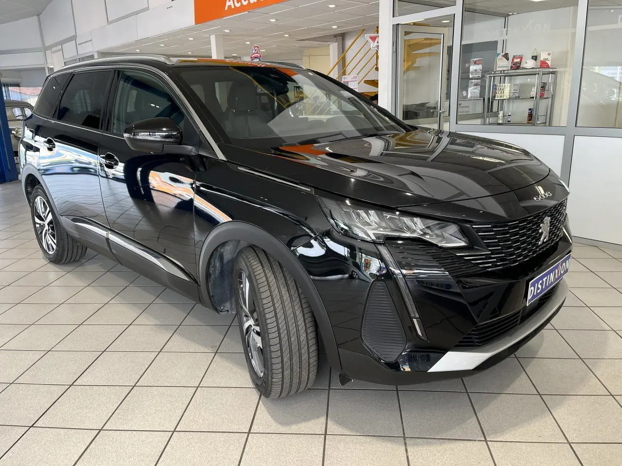 Peugeot 5008 noir métallisé en 3/4 avant droit, avec calandre à damier chromé et jantes alliage 18 pouces.