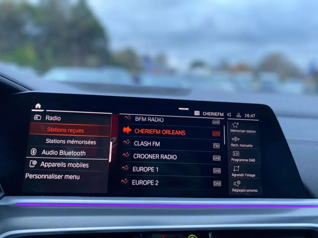 Écran tactile multimédia du BMW X5 blanc 2022, affichant les stations radio avec interface moderne et éclairage d'ambiance violet.