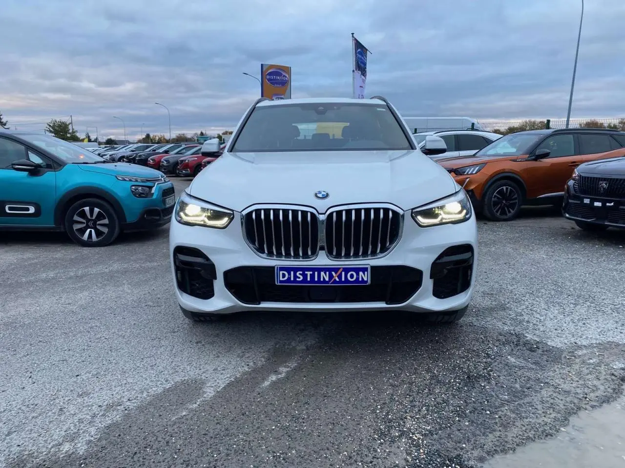 BMW X5 xDrive 30d blanc vu de face, phares allumés et calandre imposante en concession extérieure.