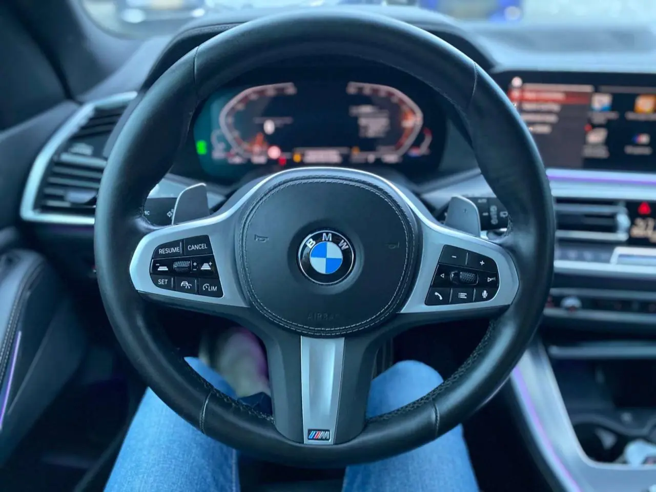 Vue intérieure centrée sur le volant M Sport noir du BMW X5 blanc xDrive 30d 2022 avec tableau de bord numérique.