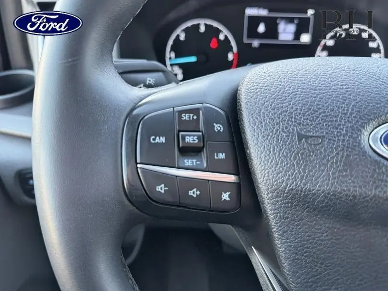 Gros plan sur les commandes au volant cuir noir du Ford Transit Custom Fourgon, avec tableau de bord en arrière-plan.