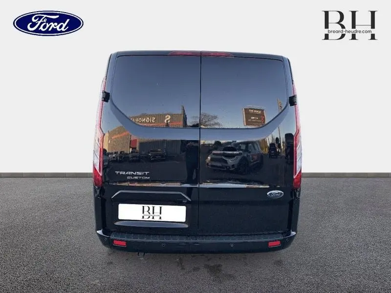 Vue arrière d’un Ford Transit Custom noir Agate métallisé avec portes battantes et logo Ford visible.