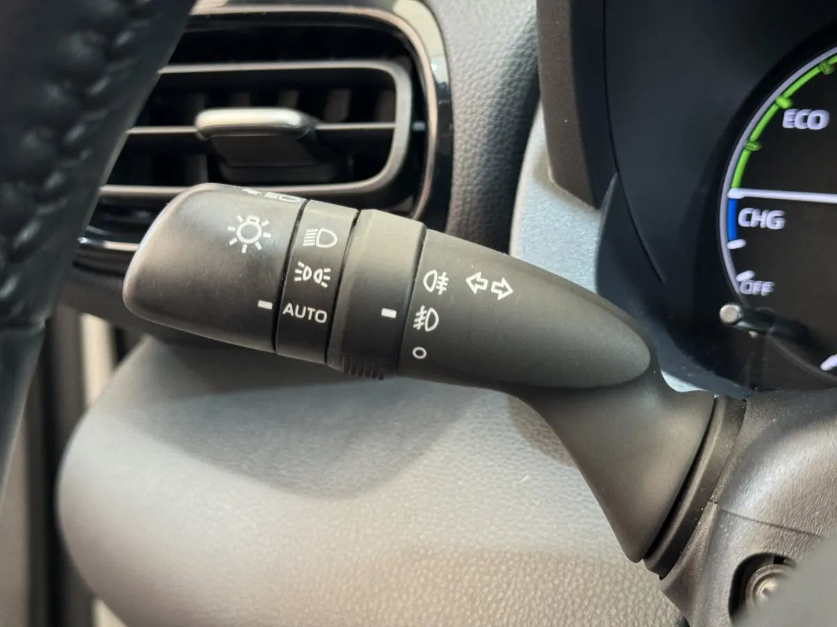 Gros plan sur la commande des phares et clignotants à gauche du volant dans l’habitacle de la Toyota Yaris hybride blanche.