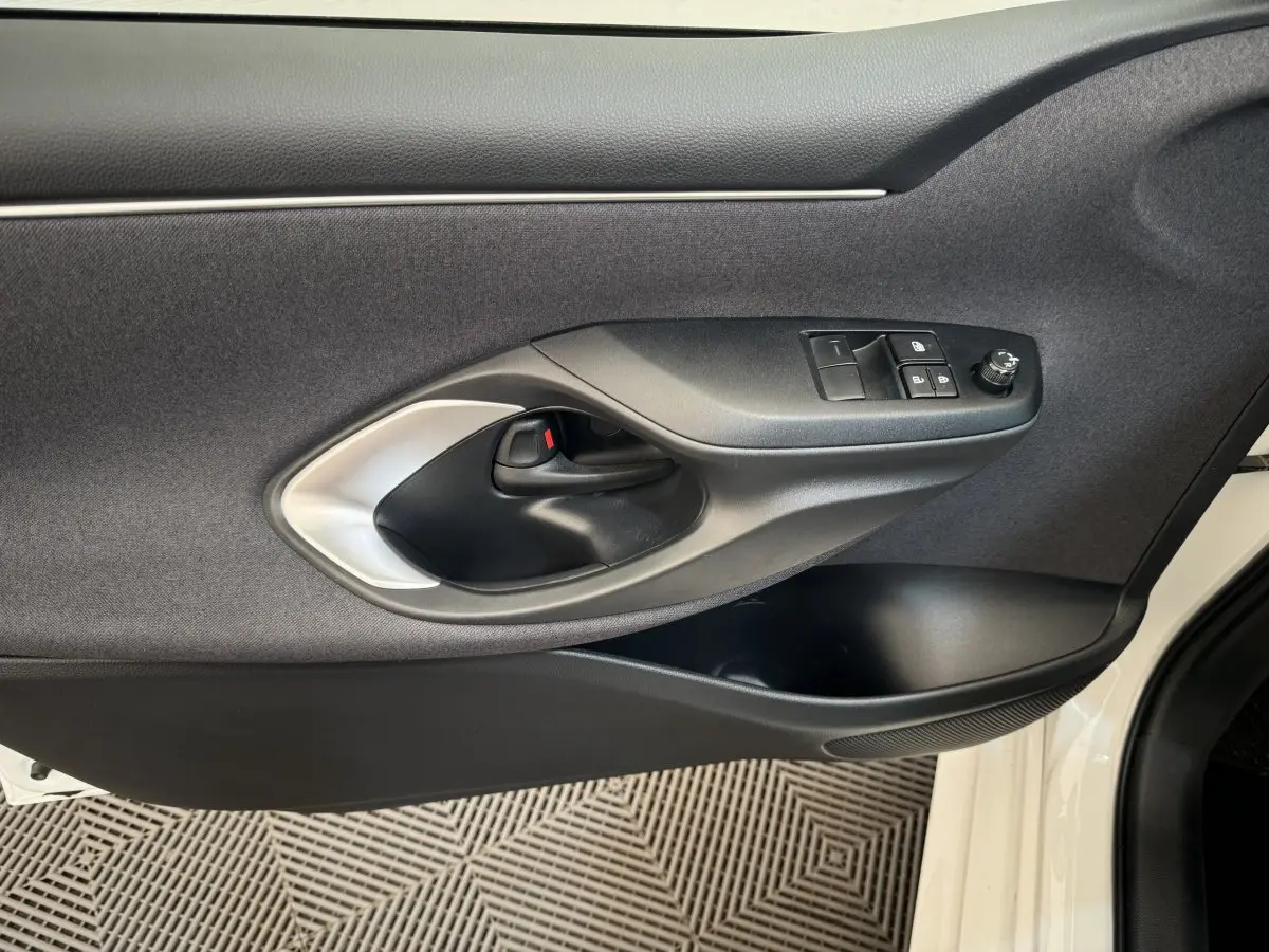 Vue intérieure côté gauche de la porte avant blanche de la Toyota Yaris hybride 2022 avec commandes de vitres et poignée noire.