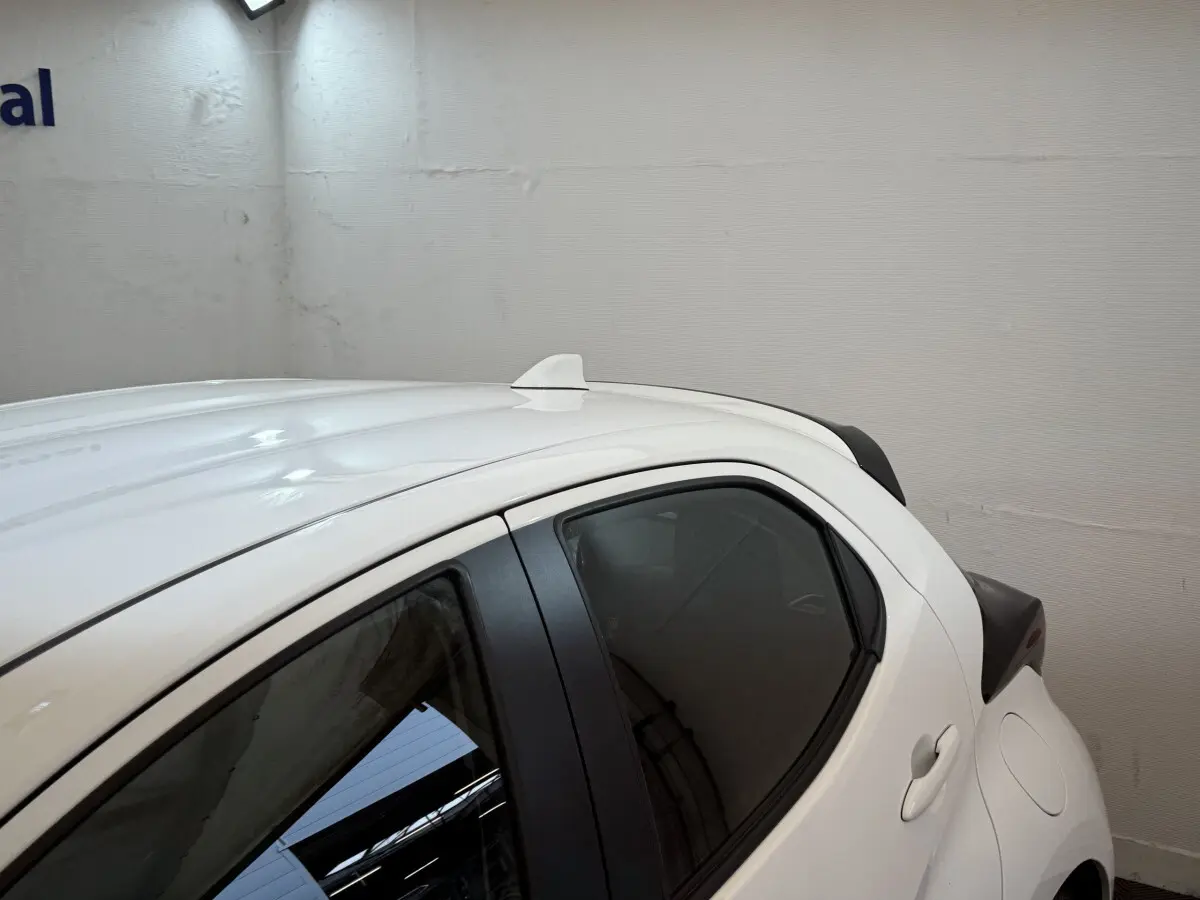 Vue latérale droite arrière d'une Toyota Yaris hybride blanche avec antenne requin sur le toit.