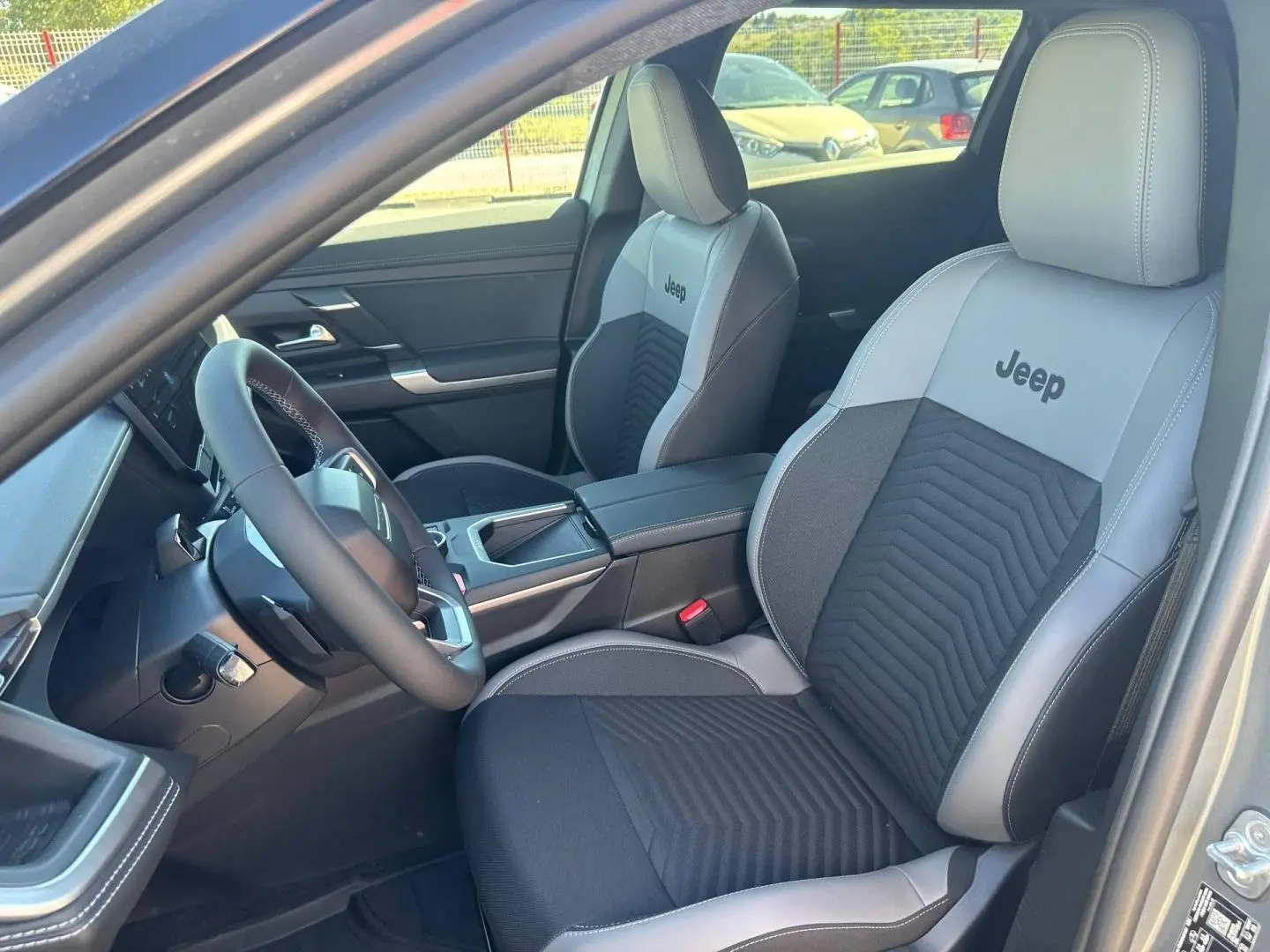 Vue intérieure côté conducteur du Jeep Compass 2026, sièges bi-ton gris et noir avec logo Jeep brodé.