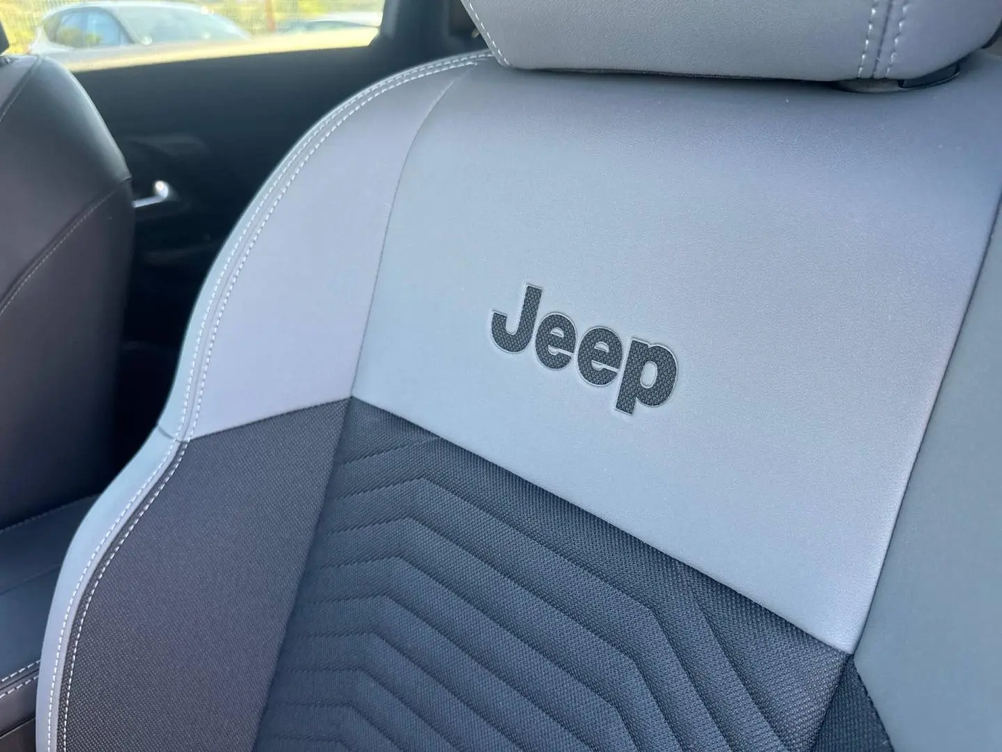 Gros plan sur le siège avant gris et noir du Jeep Compass 2026 avec logo Jeep brodé et surpiqûres blanches.
