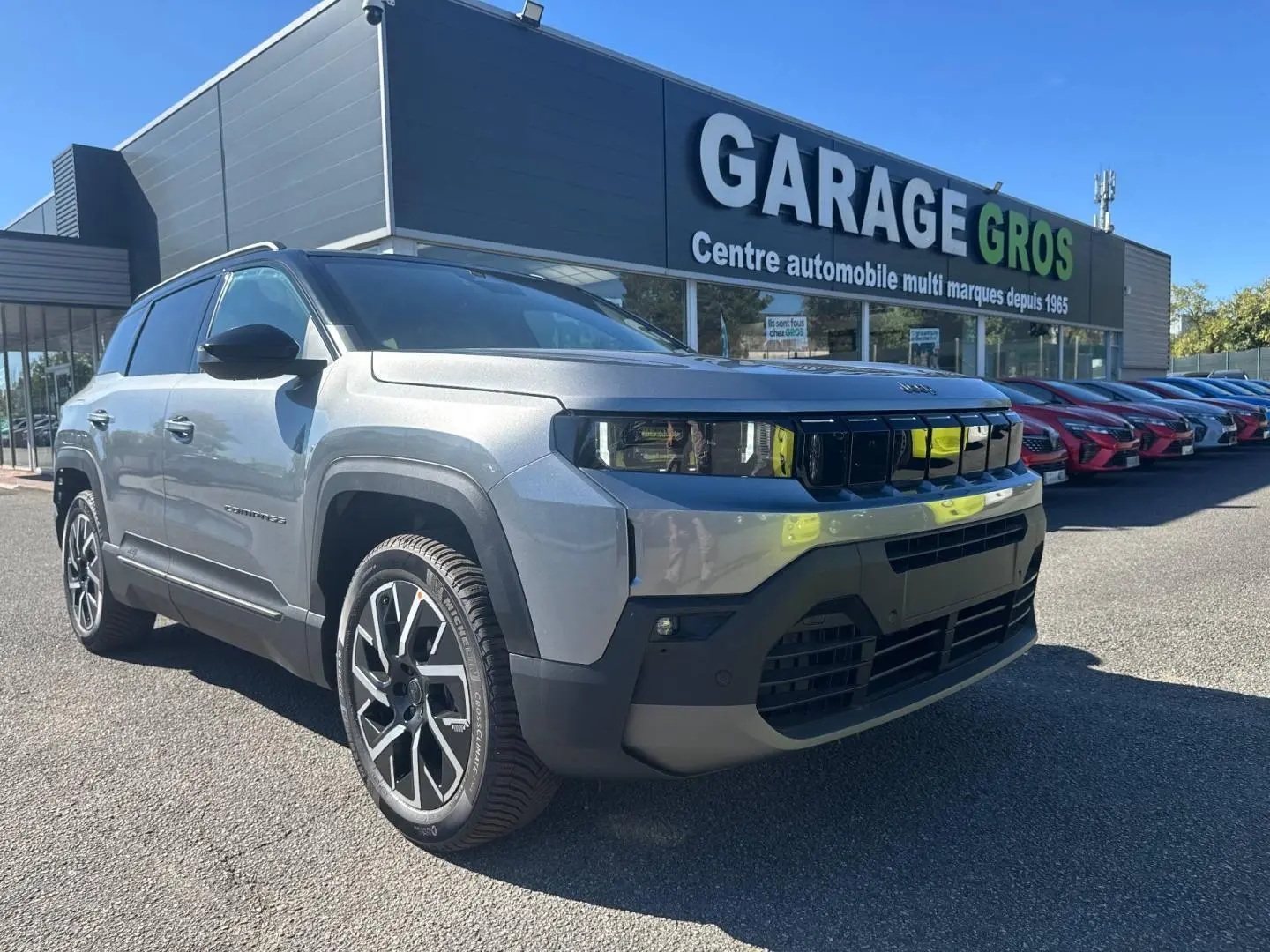 Jeep Compass Yosemite gris clair avec toit noir, vue 3/4 avant droit devant un garage automobile.