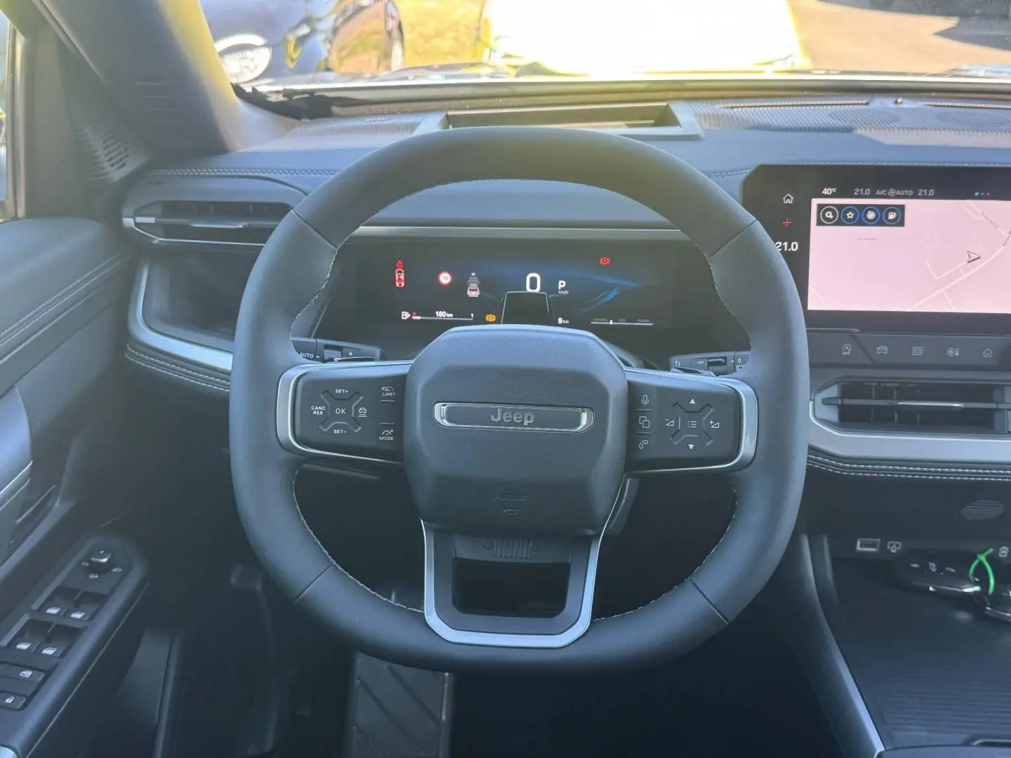 Vue intérieure centrée sur le volant Jeep noir avec tableau de bord digital et écran tactile à droite.