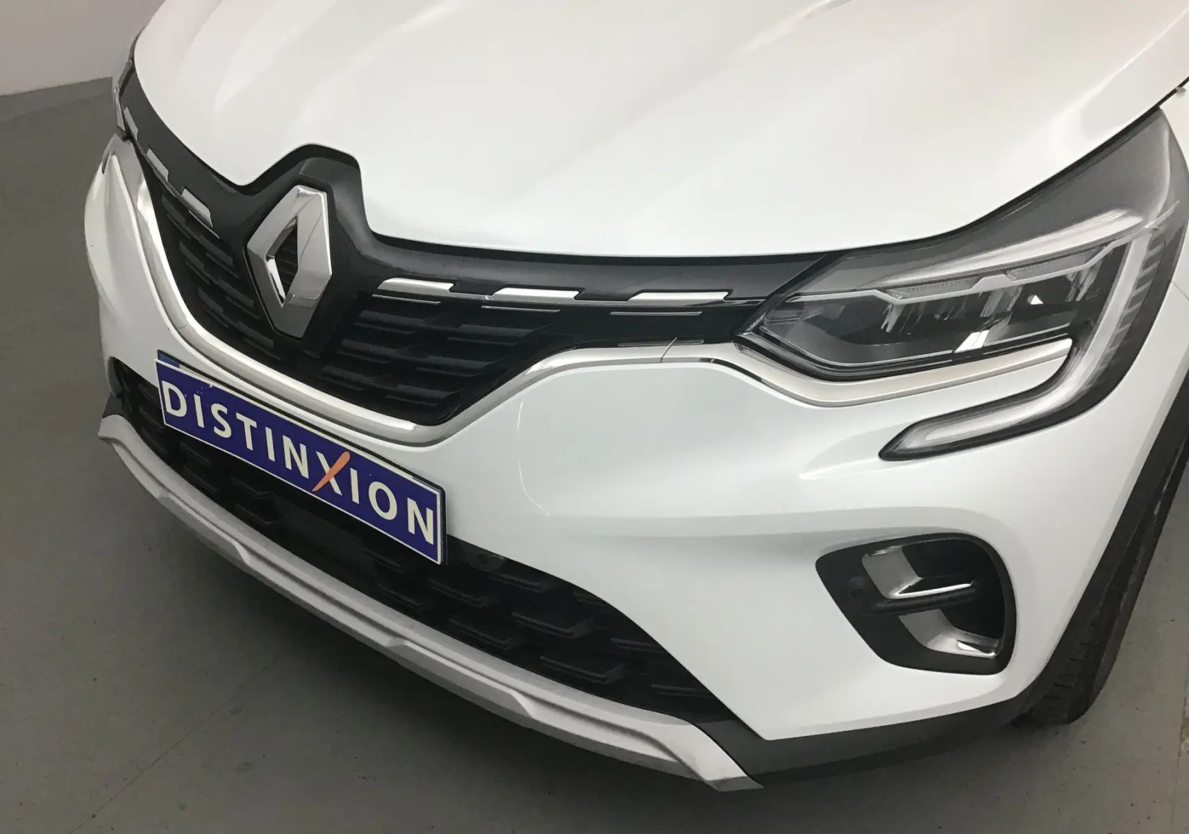 Gros plan sur l'avant droit du Renault Captur blanc nacré avec calandre noire et feux LED distinctifs.