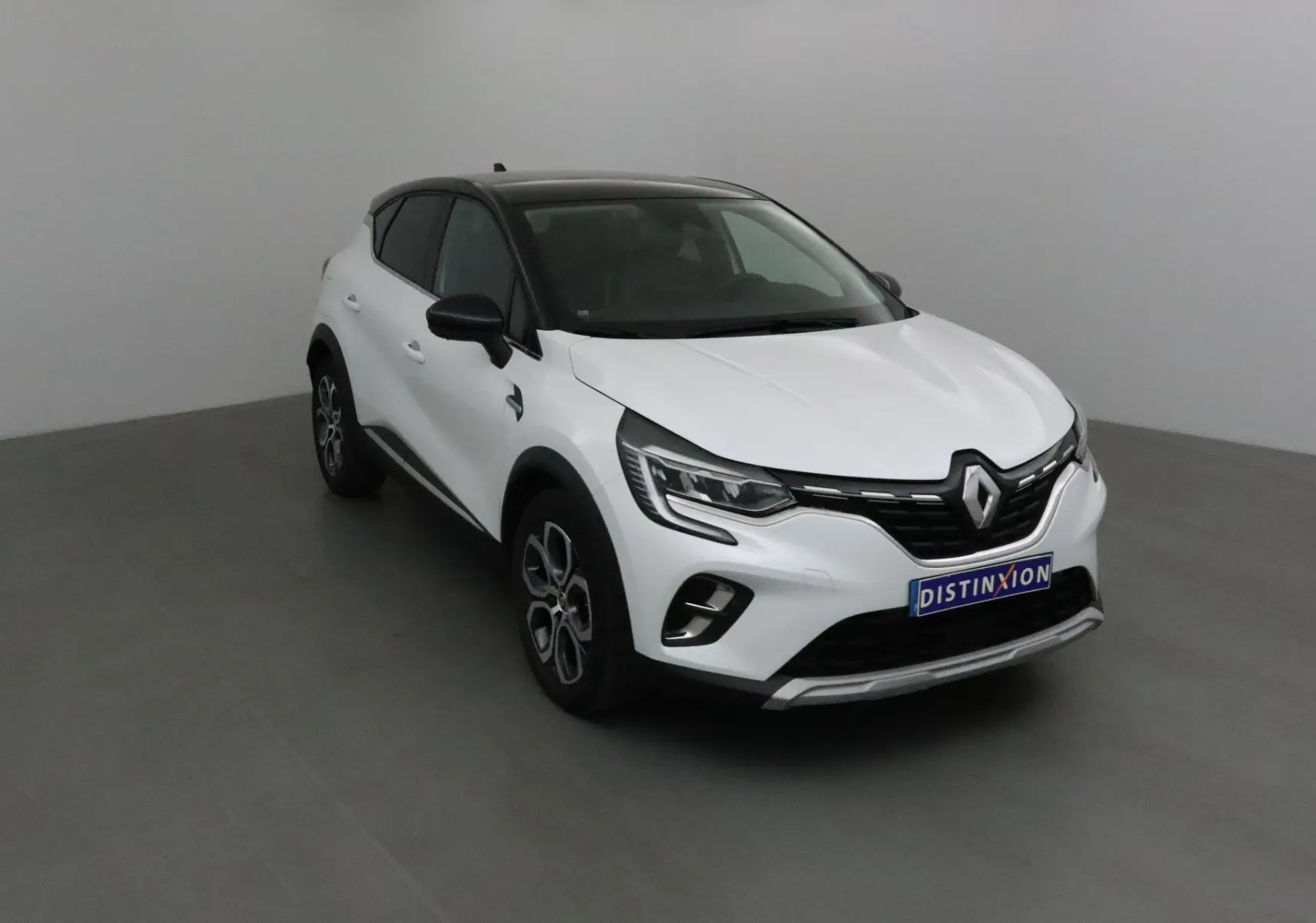 Renault Captur blanc nacré avec toit noir, vu en 3/4 avant droit dans un studio gris neutre.