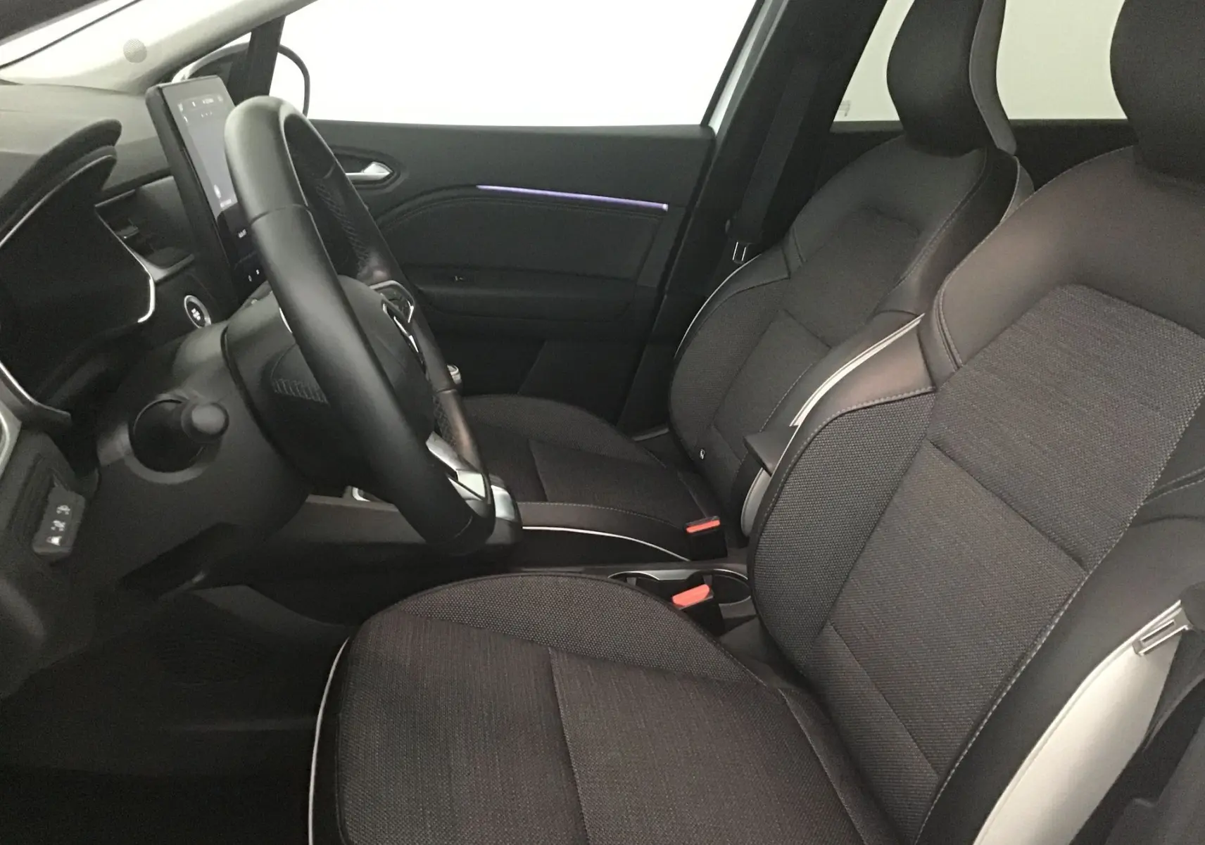 Intérieur du Renault Captur 2024 vu côté conducteur, sièges noirs avec surpiqûres claires et écran tactile vertical.