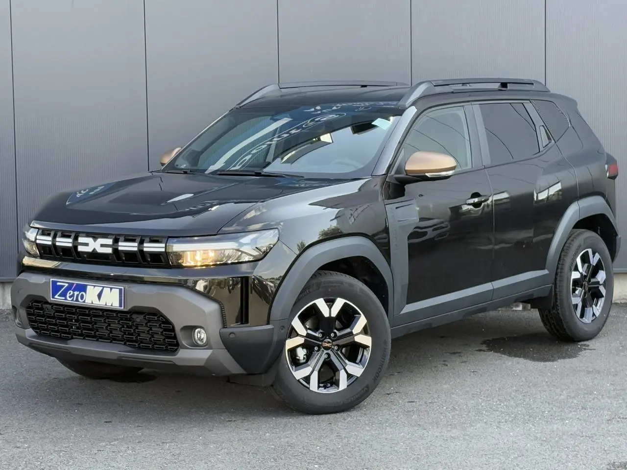 Dacia Duster noir nacré en 3/4 avant droit, avec coques de rétroviseurs brun cuivré et jantes alliage 17 pouces.