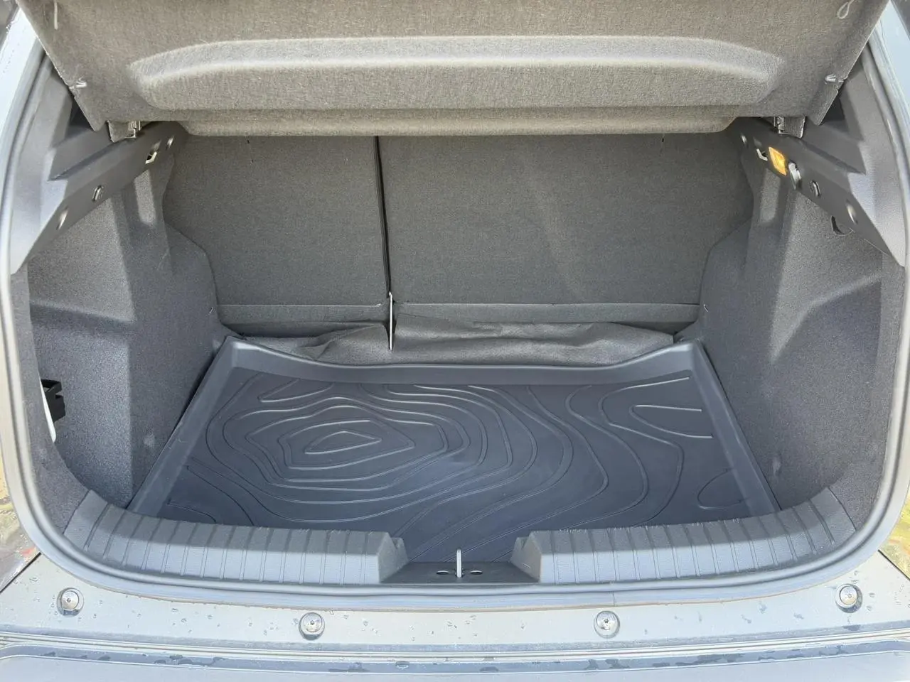Vue intérieure du coffre ouvert du Dacia Duster noir nacré 2025, montrant le tapis de protection en caoutchouc.